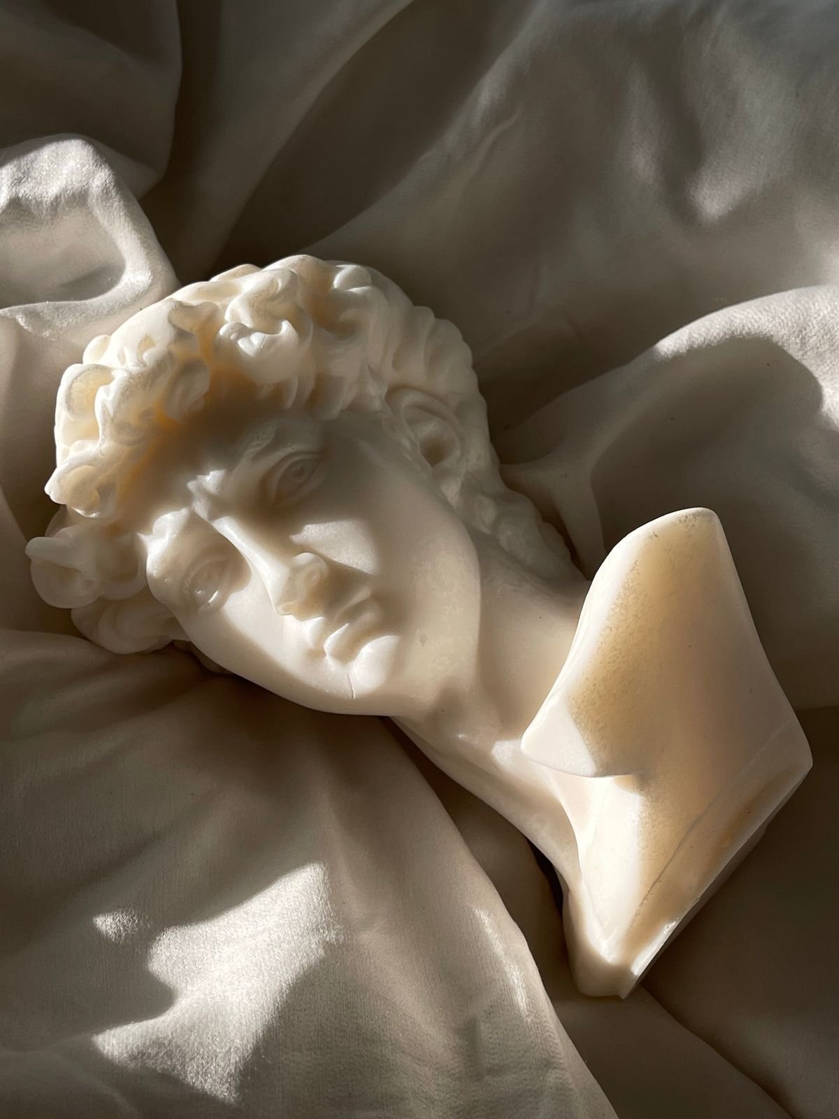 Busto de mármol blanco sobre tela clara iluminado por luz lateral.